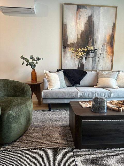 A living room with a grey couch, a green chair, and a painting on the wall.