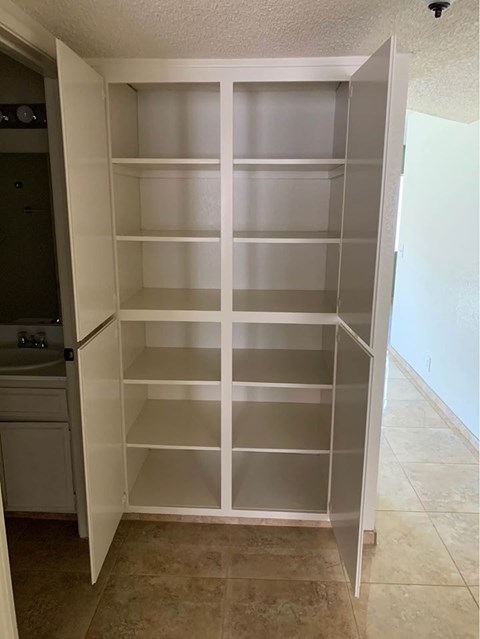 A white pantry with shelves and a door open to a bathroom.
