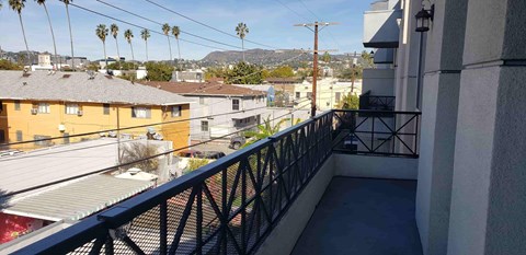 A balcony with a black railing overlooks a street with houses and palm trees.
