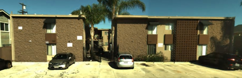 A black car is parked in front of a tan building.