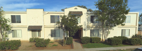 A white building with a brown roof and a tree in front.