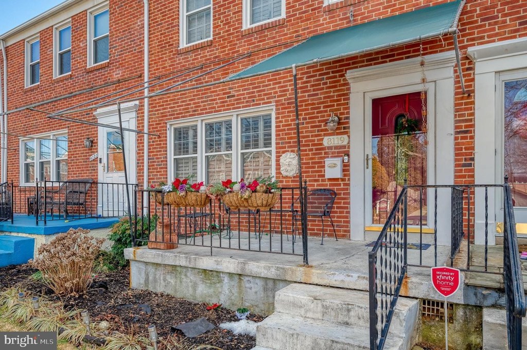 A red brick house with a green awning and a red sign on the stairs.