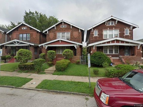 A red car is parked in front of a brick house.