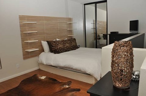 A bedroom with a bed, a cowhide rug, and a tall vase on a table.