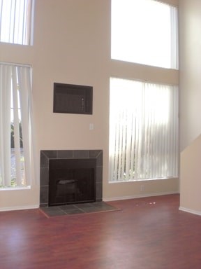 A black fireplace in a room with wooden floors and a window.