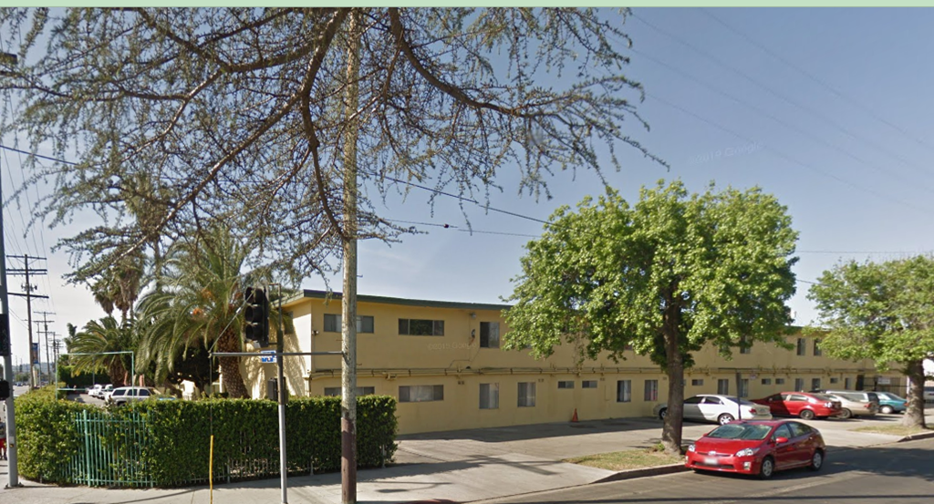 A street view of a yellow building with a red car parked in front.