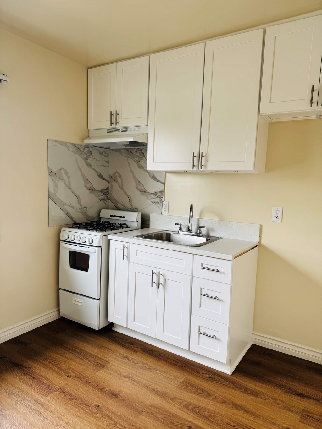 A kitchen with a white stove, sink, and cabinets.