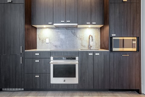 A modern kitchen with dark wood cabinets and a marble backsplash.