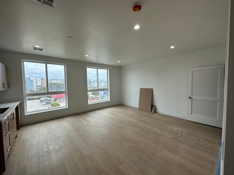 A large empty room with wooden flooring and a view of the city through the windows.