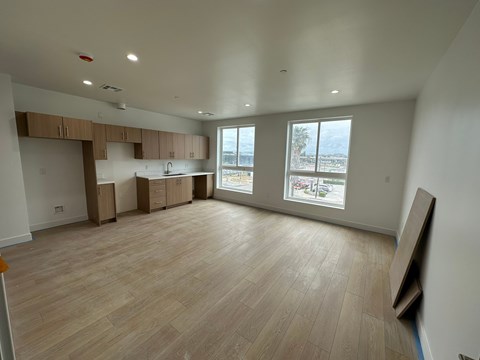 A large empty room with wooden flooring and a kitchen area in the background.