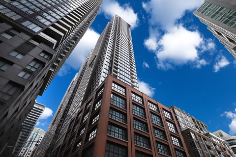 A tall building with a glass facade stands in front of other buildings.