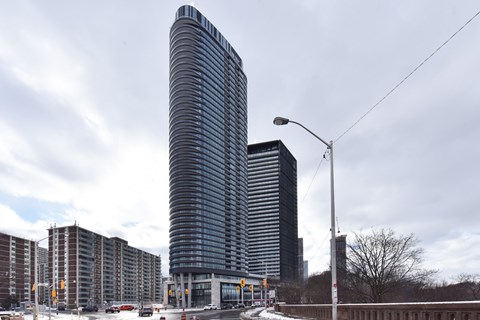 A tall, curved building stands in front of a row of shorter buildings.