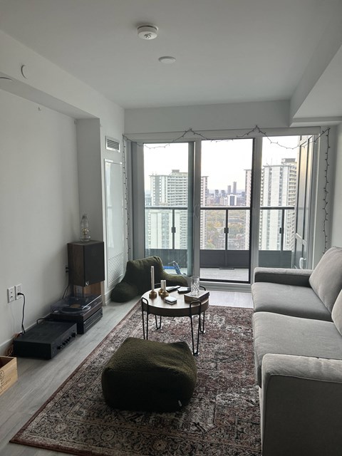 A living room with a grey couch, a coffee table, and a large window with a view of the city.