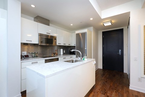 A modern kitchen with white cabinets and a wooden floor.