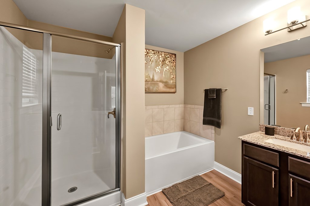 A bathroom with a glass shower door, a white bathtub, and a brown rug.