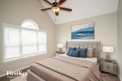 A bedroom with a large bed, a ceiling fan, and a painting of a wave on the wall.