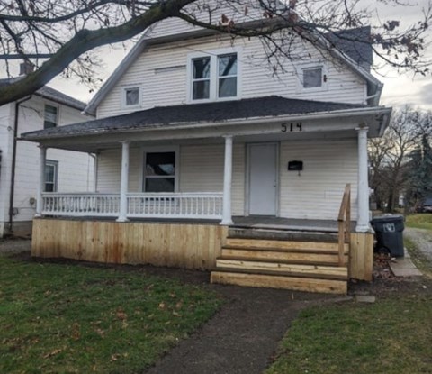 A white house with a porch and a tree in front.