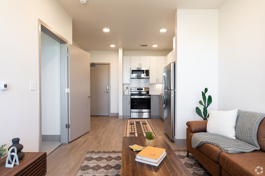 A modern living room with a couch, coffee table, and kitchen area in the background.