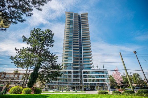A tall, modern building with many windows and balconies is surrounded by trees and greenery.