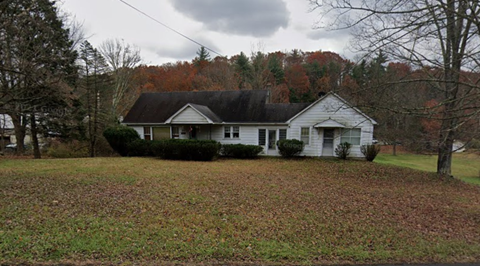 A white house with a black roof is surrounded by trees with autumn leaves.
