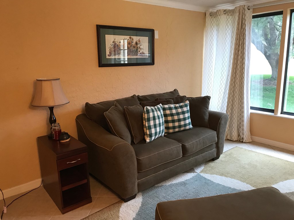 A brown couch with a checkered pillow is in front of a window with curtains.
