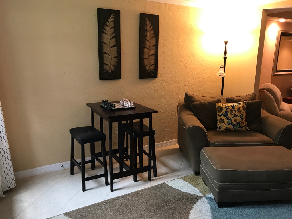 A living room with a couch, chair, and a small table with a chess set on it.