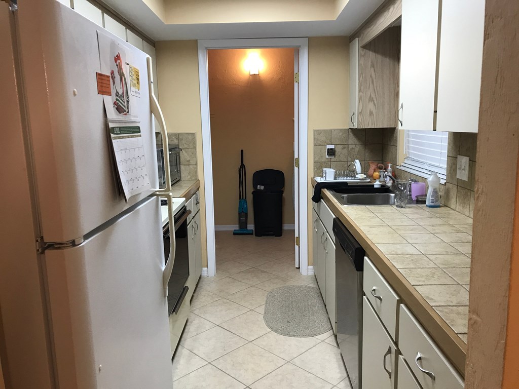 A kitchen with a white fridge and a black vacuum cleaner.
