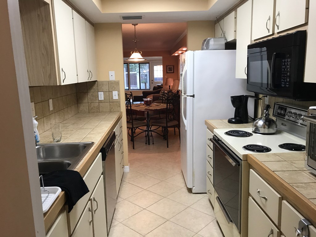 A kitchen with a white refrigerator, black microwave, and a dining table with chairs.