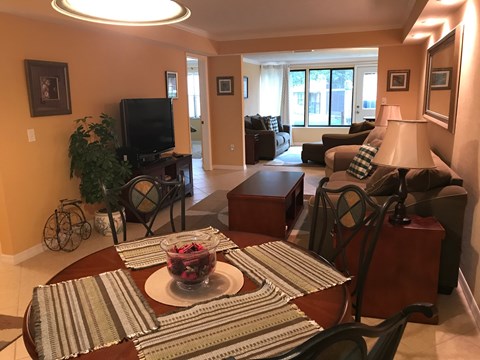 A living room with a television, couches, and a dining table with a bowl of fruit on it.