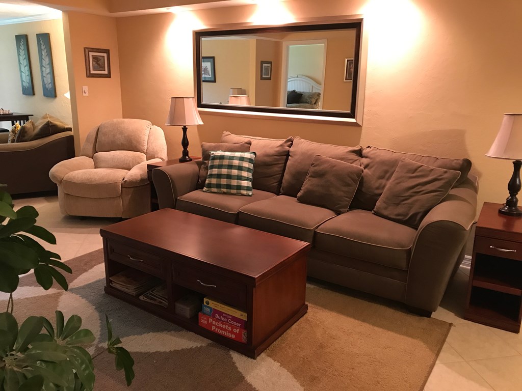 A living room with a brown couch, a chair, a coffee table, and a mirror.