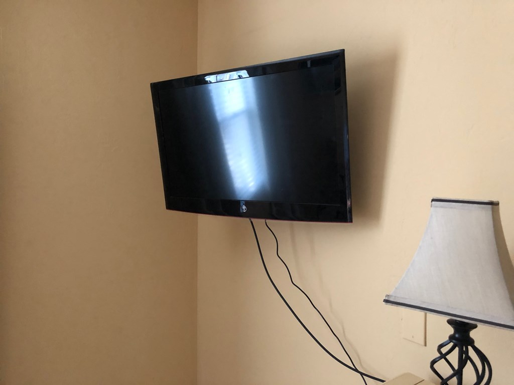 A black flat screen TV is mounted on a wall above a white lamp.