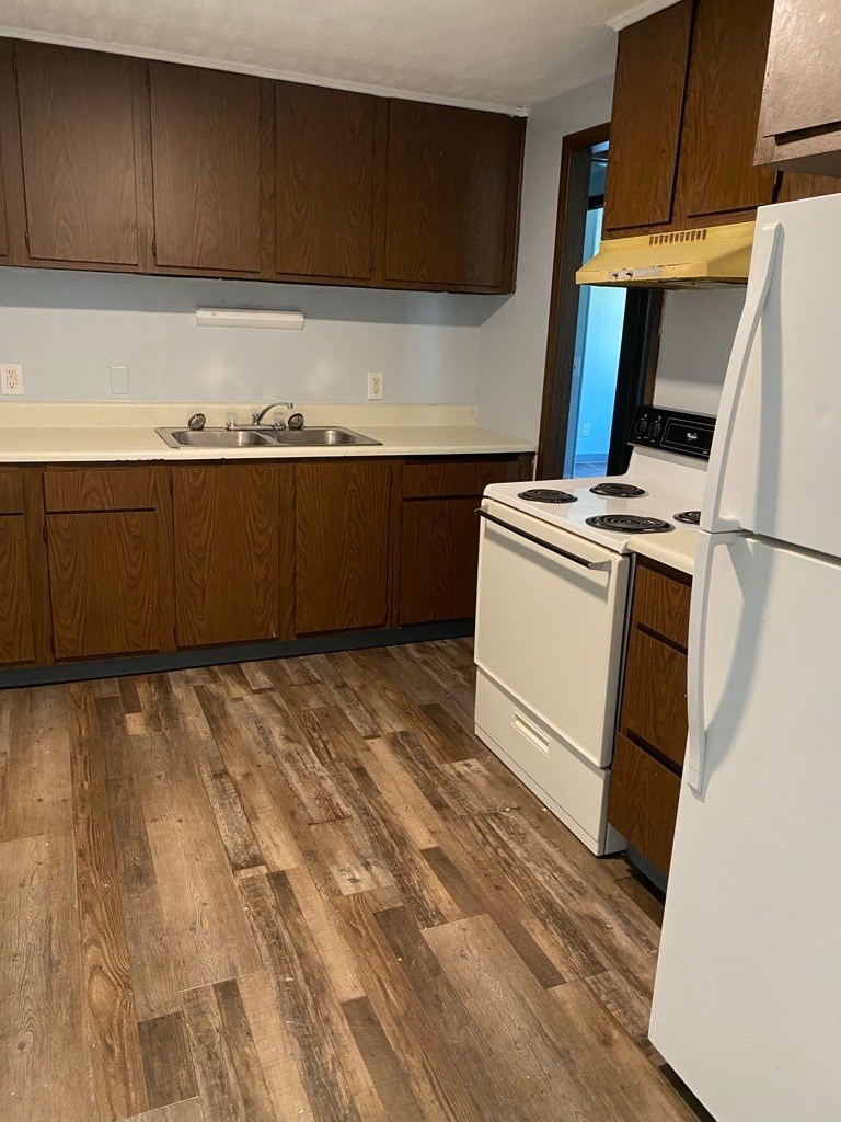 A kitchen with a white fridge and wooden floors.