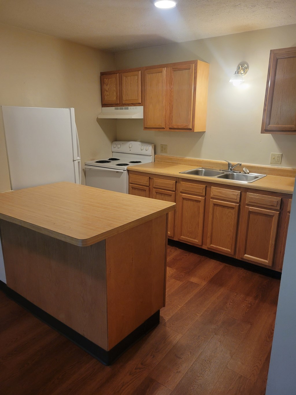 A kitchen with a white fridge, white stove, wooden cabinets and a wooden island.