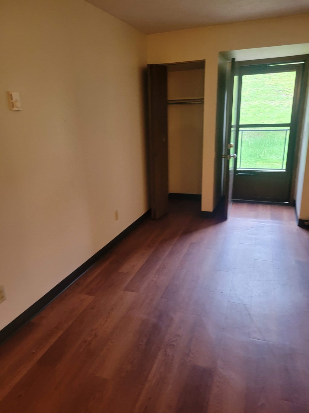 A room with a wooden floor and a door leading outside.