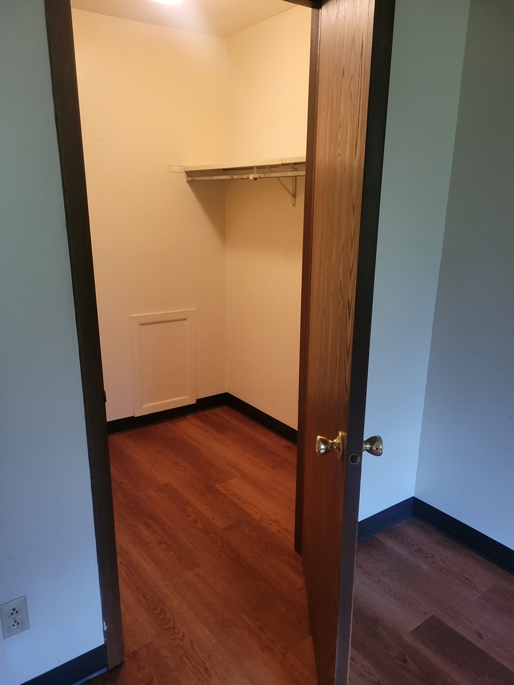 A hallway with a door on the right and a shelf on the wall.