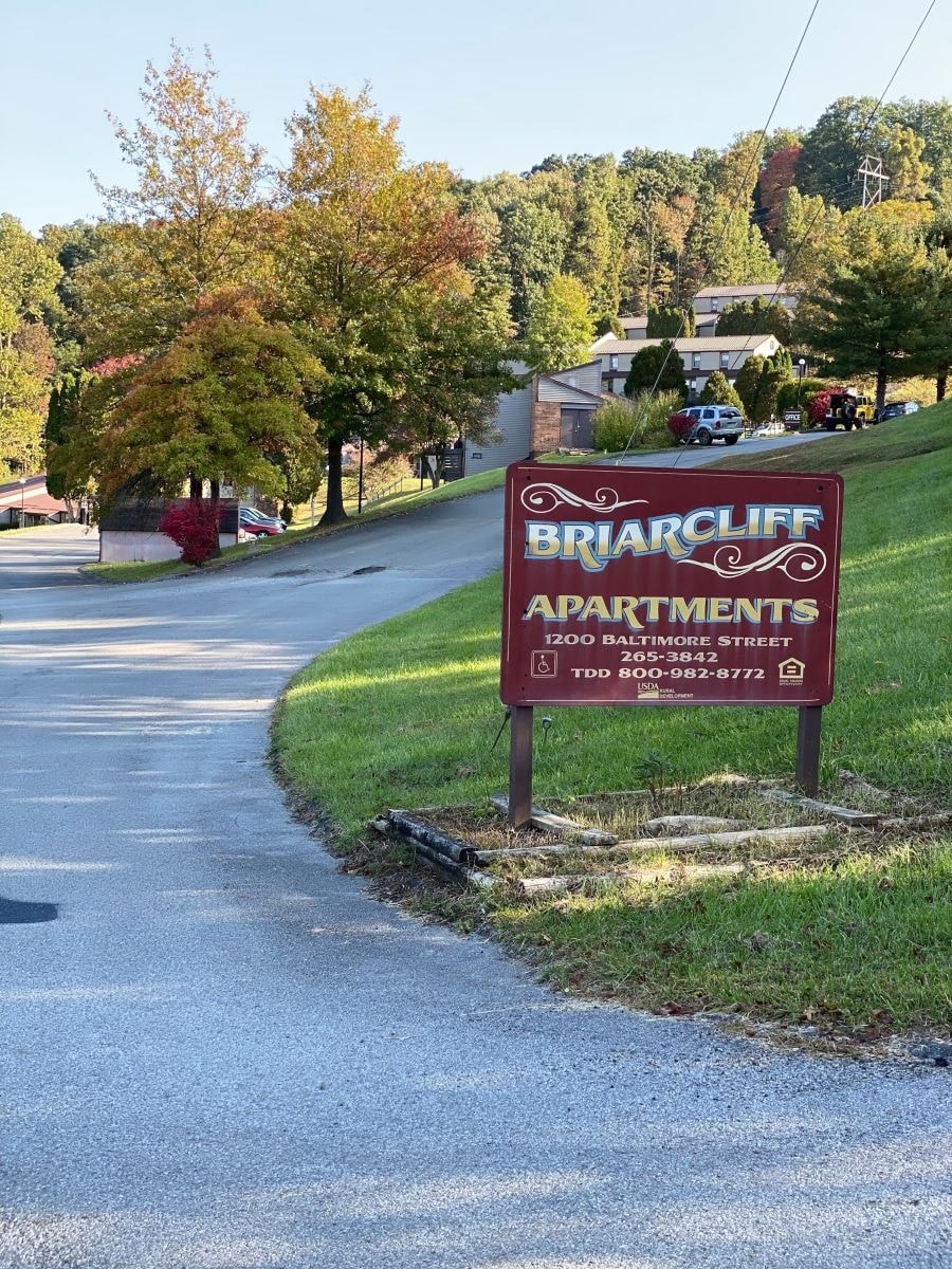 A sign for Briarcliff Apartments is on the grass beside a road.