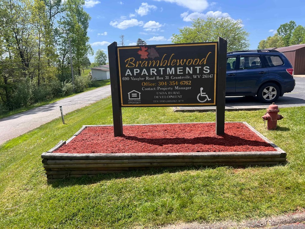A sign for Bramblewood Apartments is displayed on a red mulch bed.