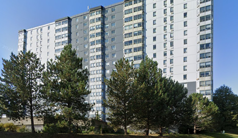 A tall building with many windows is surrounded by trees.