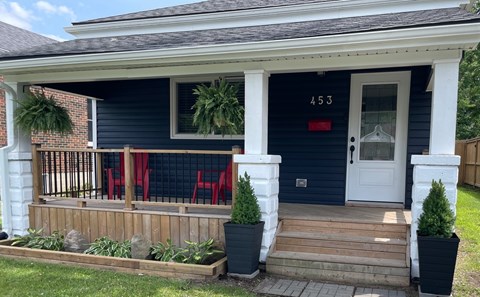 A blue house with a white door and red chairs on the porch.