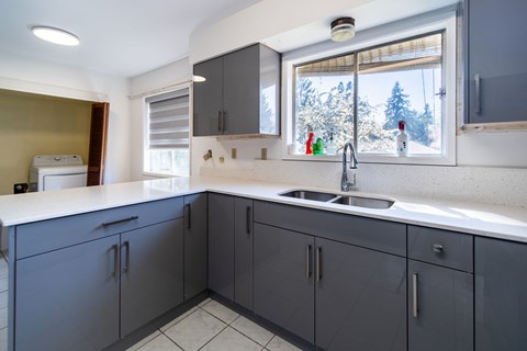 A kitchen with grey cabinets and a white countertop.