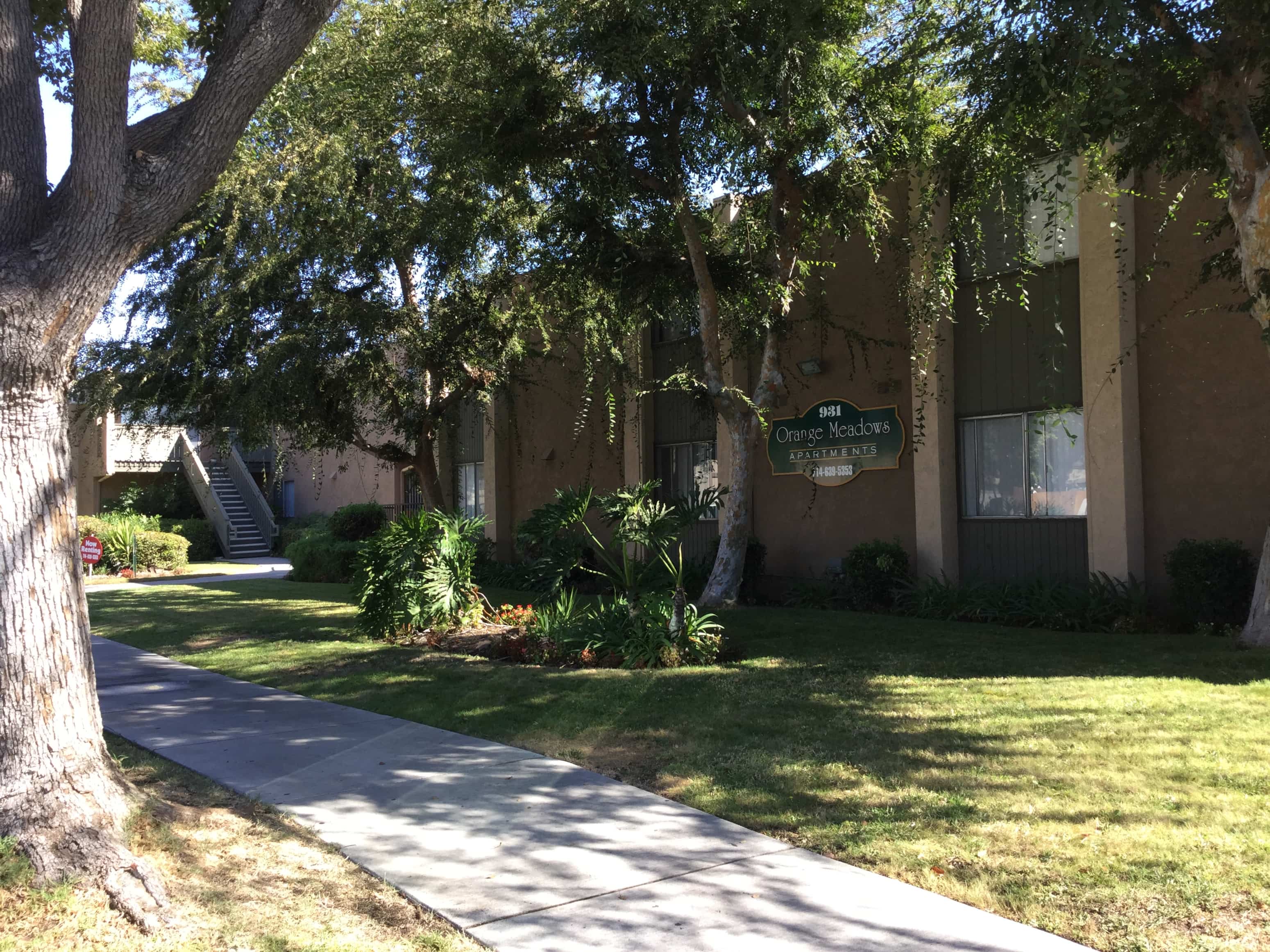 A tree-lined sidewalk in front of a building with a sign that reads "Orange Heights.".