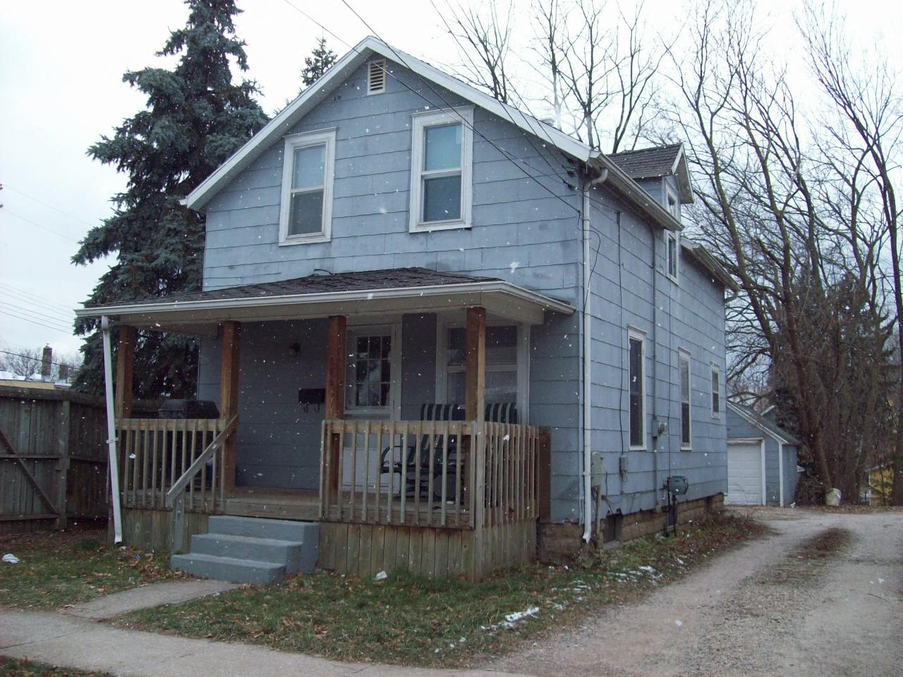 A blue house with a porch and a dirt road in front.