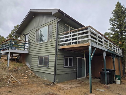 A house under construction with a grey exterior and a wooden deck.