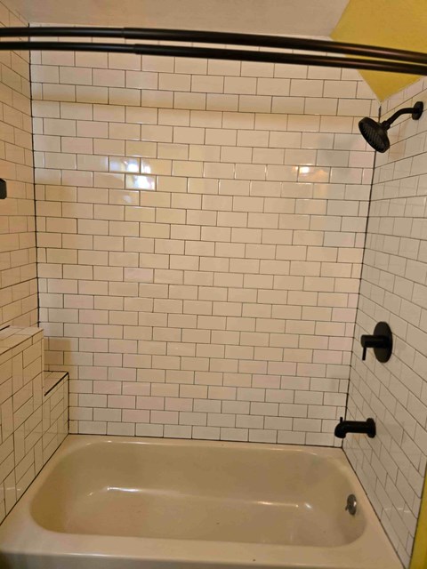 A white tiled shower with a black handle and a white bathtub.