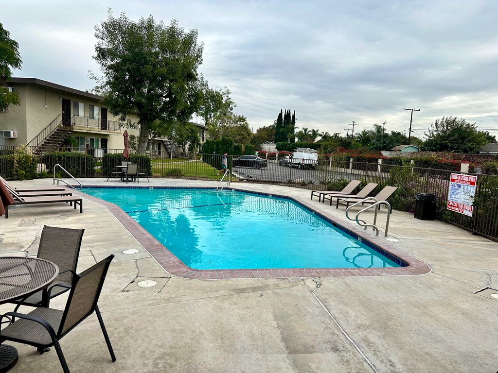 A pool surrounded by a concrete patio and a black metal fence.