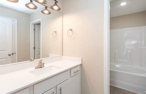 A white bathroom with a sink, mirror, and a bathtub.