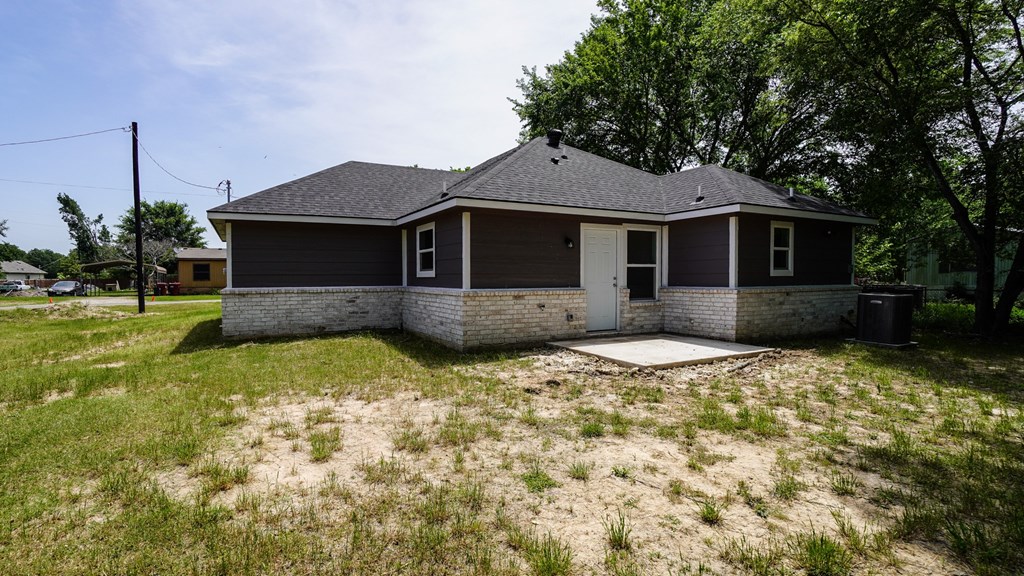 A house with a brown roof and a grey wall is surrounded by a grassy area.