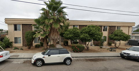 A white car is parked in front of a house with a palm tree.