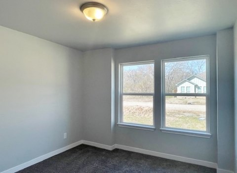 A room with a grey carpet and two windows.