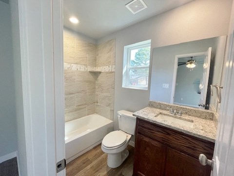 A bathroom with a white toilet, a white bathtub, and a marble countertop.